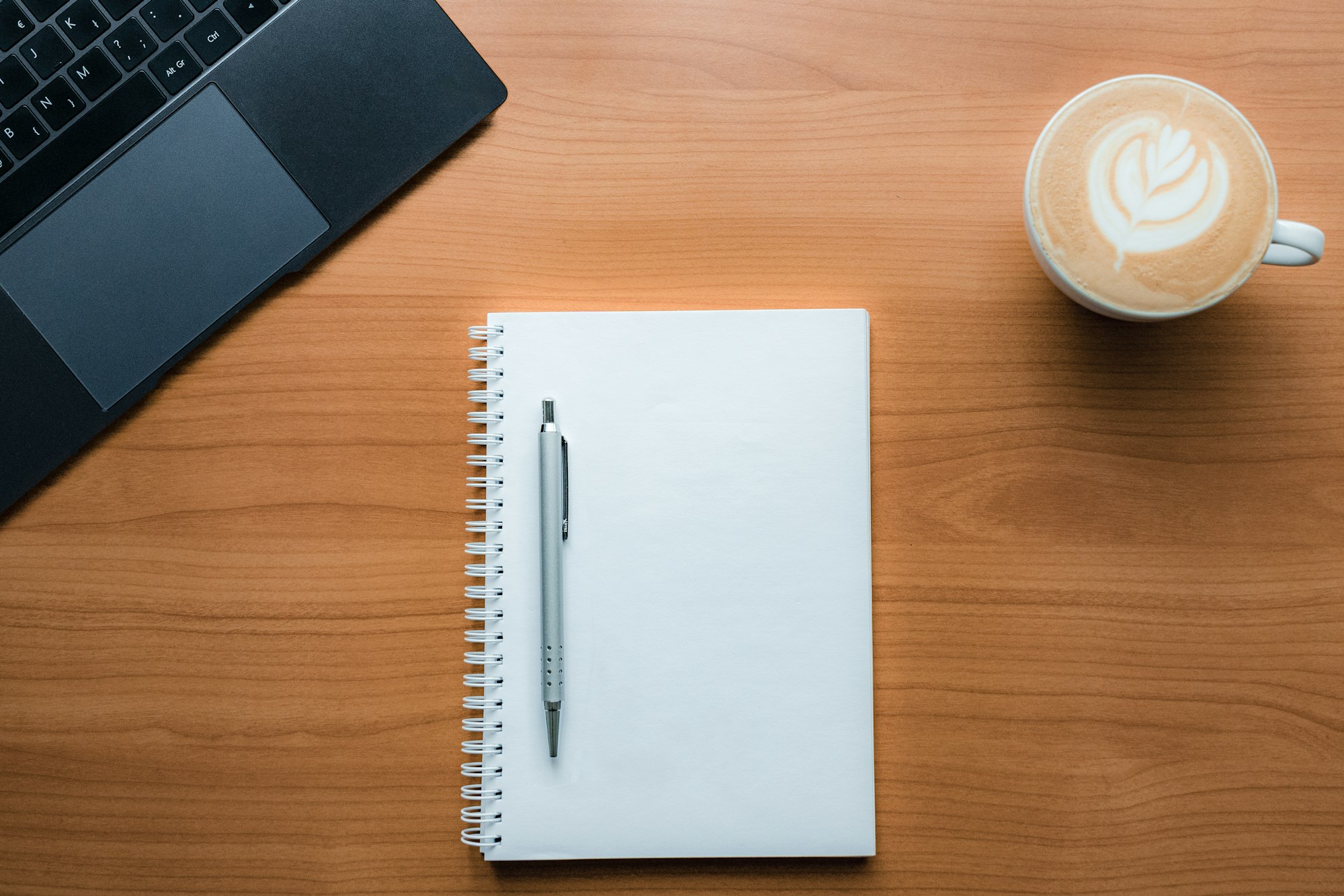 A notebook, pen and coffee on a wooden desk