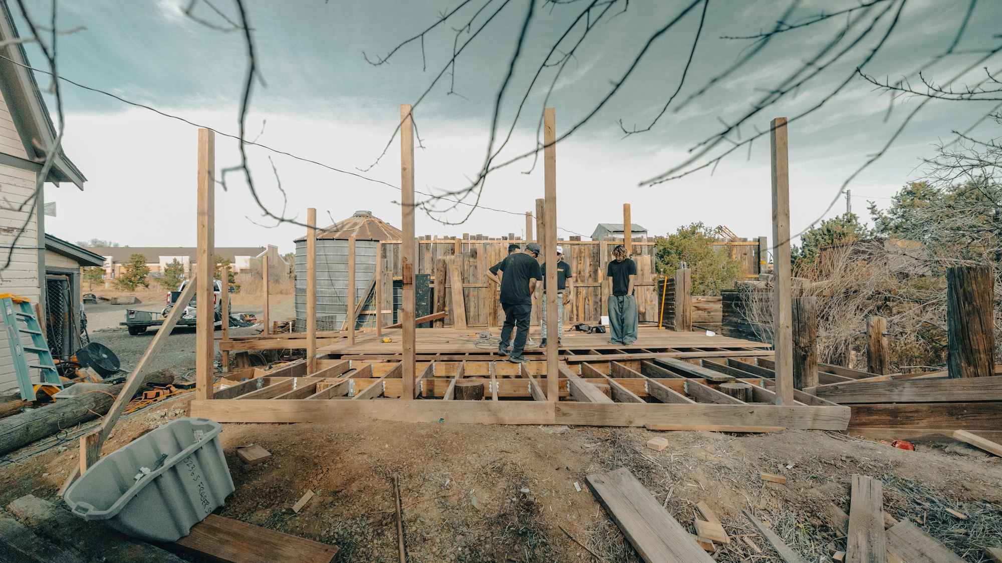 Three workers building a timber deck frame in a rural yard