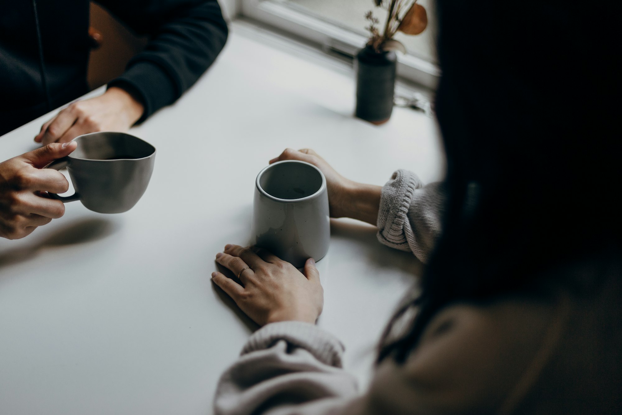 Two people talking over coffee at a table by a window