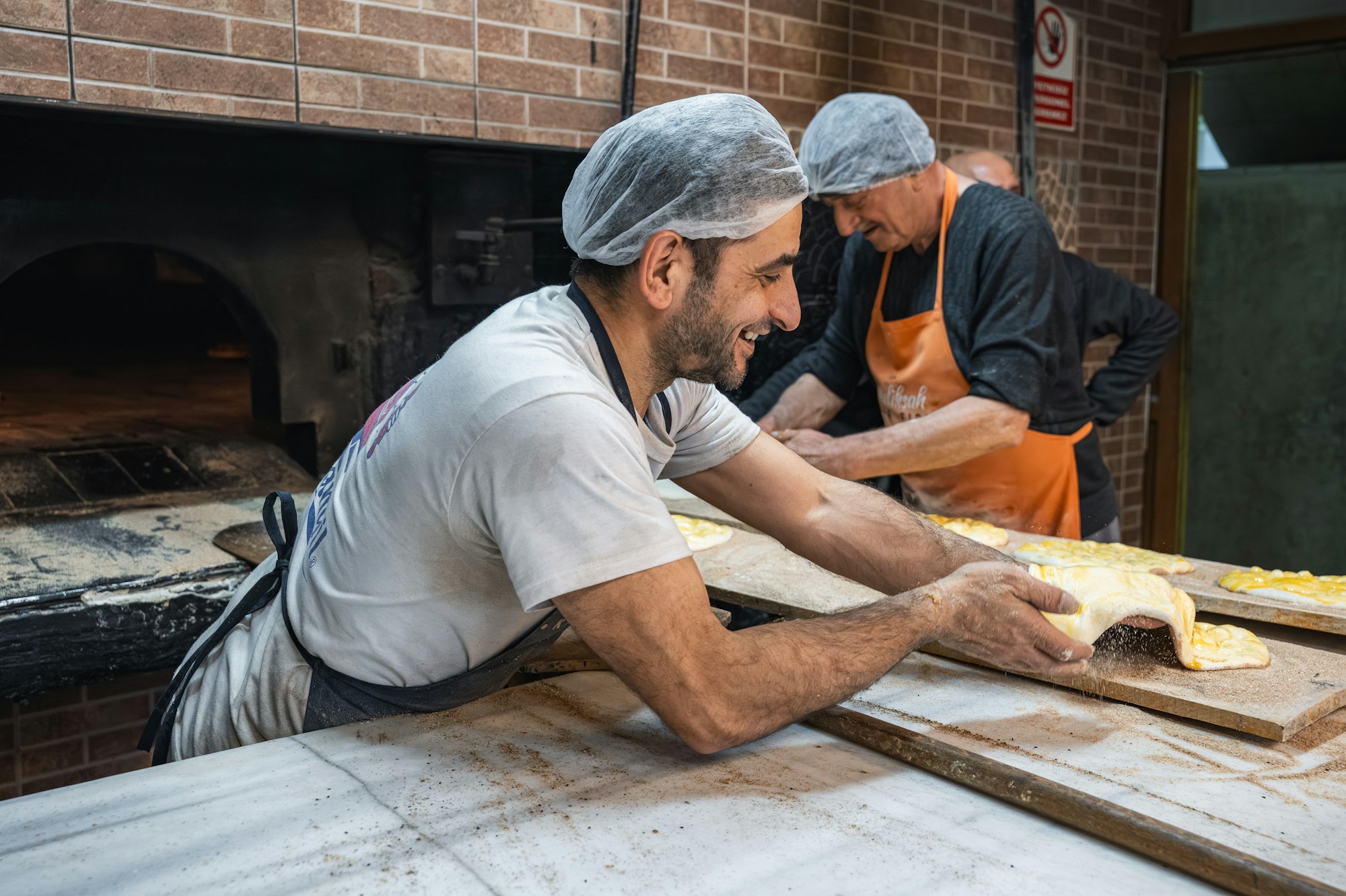 Two bakers shaping bread beside a brick oven