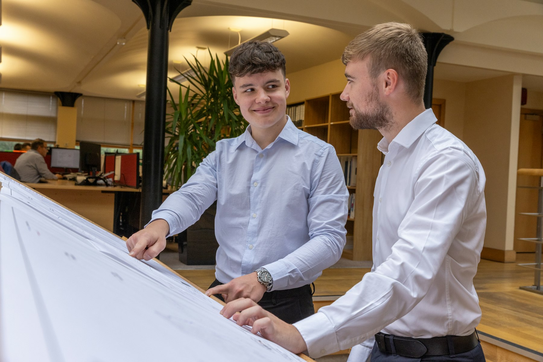 Two engineers reviewing drawings at a drafting table in their office