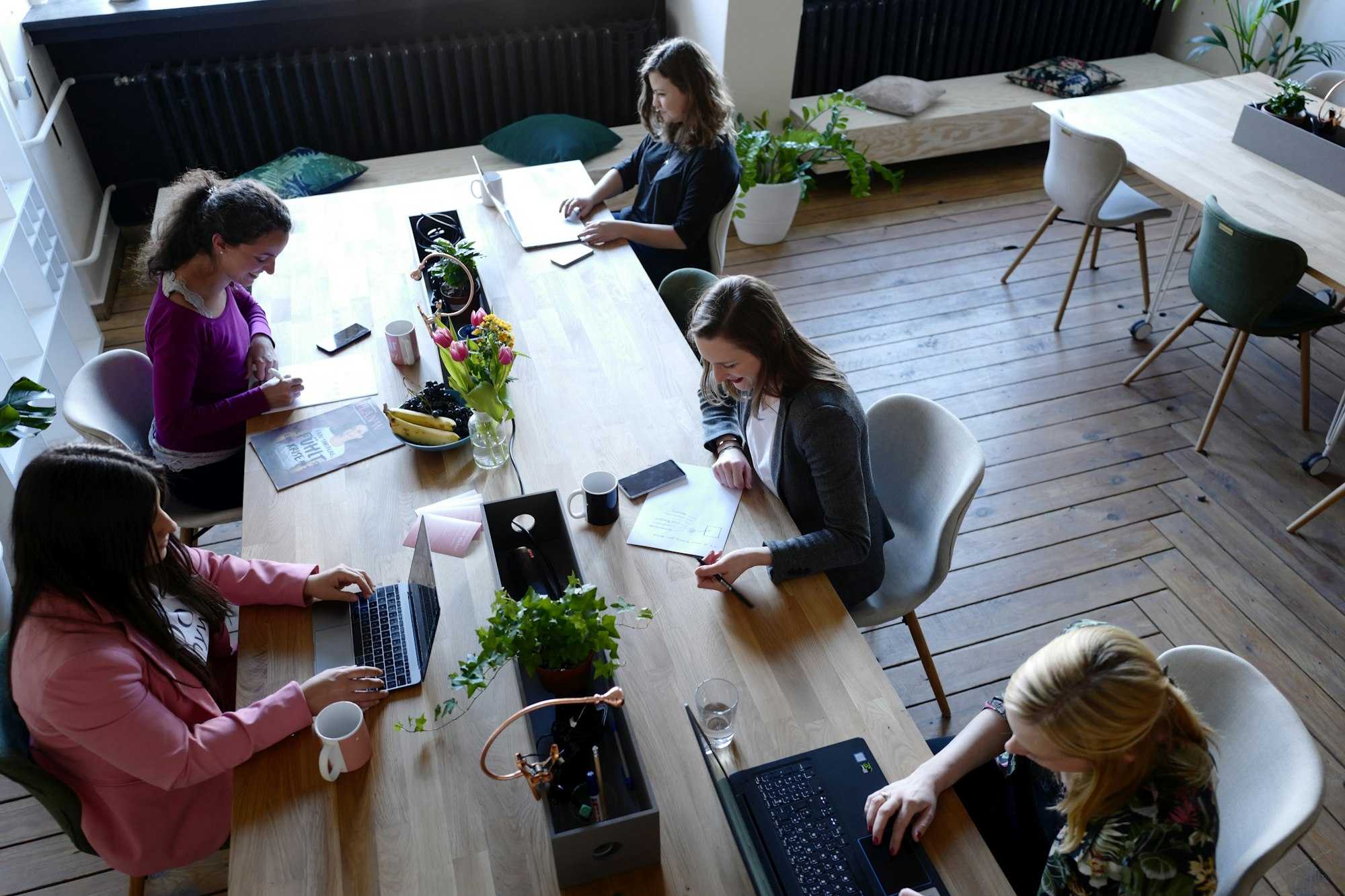 A small team working together at a long wooden table with laptops and notebooks