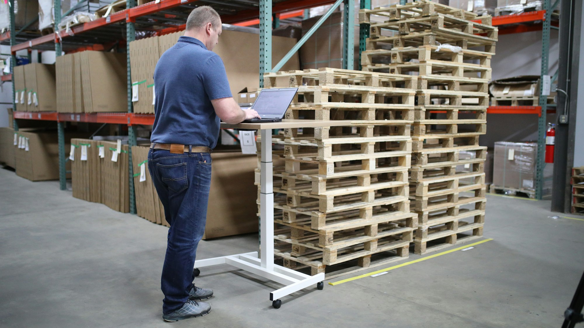 A man logging stock on a laptop beside warehouse shelves